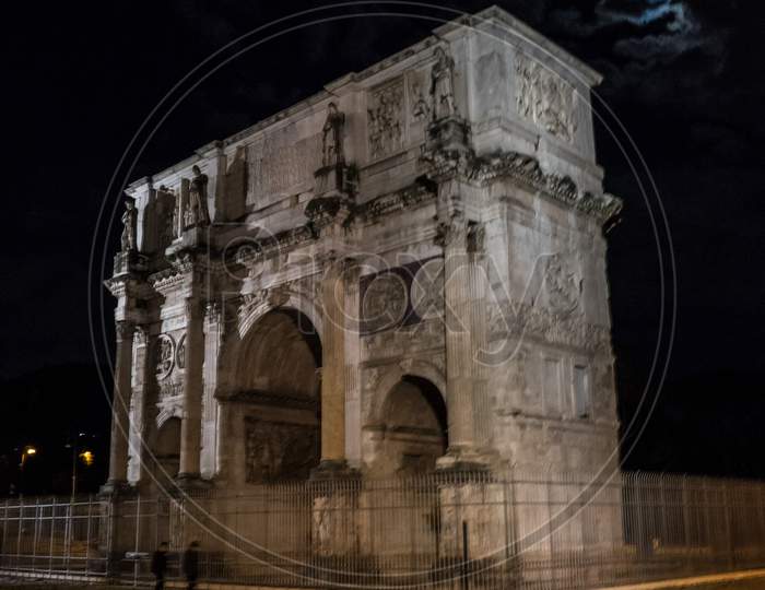 Arch Of Constantine Of The Roman Forum Viewed Through The Gated Arch Of The Passage At The Entrance Of The Roman Colosseum At Night.
