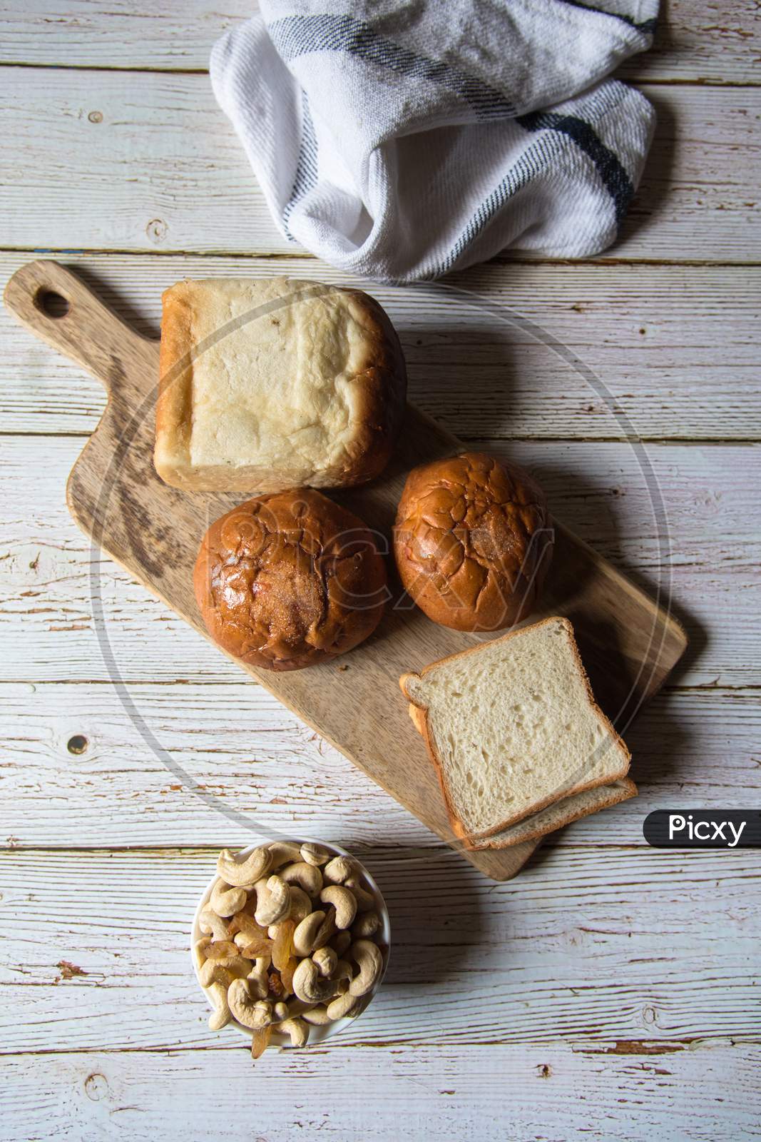 Top view of still life with bread, dry fruits and buns on a wooden platter