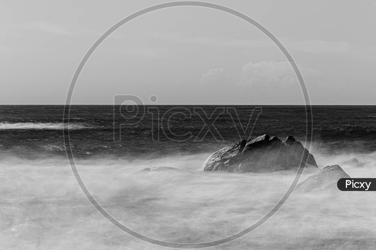 Long Exposure Black And White Shot Of A Rock In The Middle Of The Wild Sea With A Bright Horizon