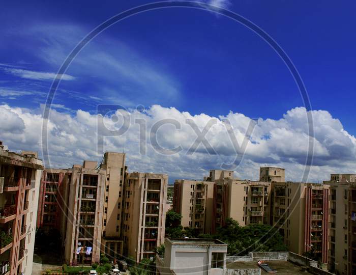 Urban landscape with buildings and white clouds in sky. Beautiful cloudscape. High sky scenery. Sunny day summer weather.