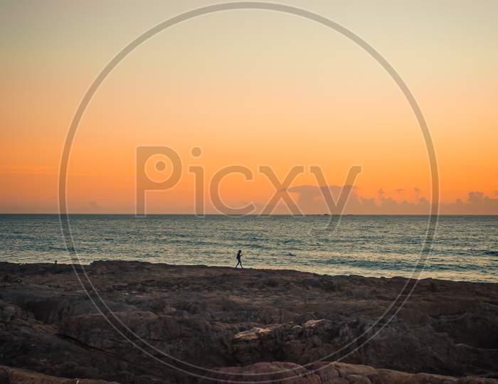 Single Person Over A Massive Rocks In Front Of The Sea With A Sunset Over The Horizon