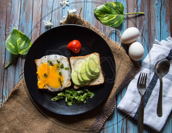 Fried egg and fresh vegetables on bread in a black plate on a background