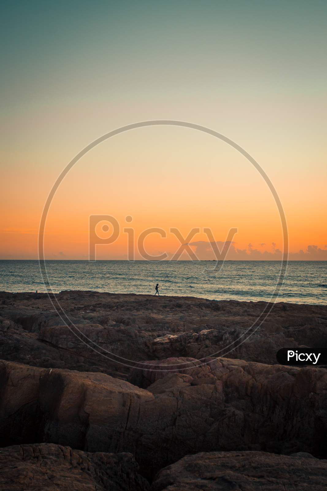 Single Person Over A Massive Rocks In Front Of The Sea With A Sunset Over The Horizon
