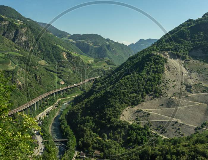 Italy, Train From Bolzano To Venice, A View Of A Lush Green Hillside With Elevayed Highway