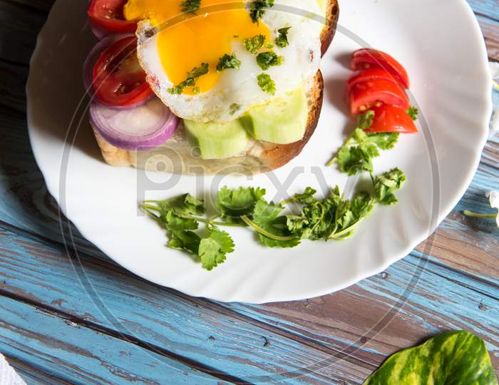 Vertical view of fried eggs with bacon and vegetables on bun bread