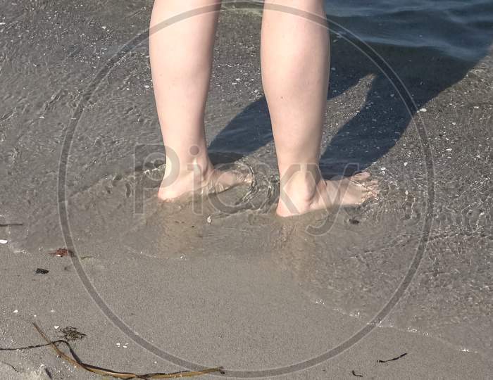 Young Female Feet Walking In The Shallow Water At A Baltic Sea Beach In Summer
