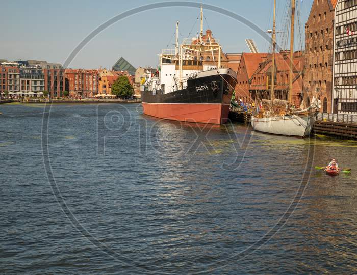 Gdansk, North Poland - August 13, 2020: A Ship Docked At Shipyard, People Enjoying Kayak In Motlawa River During Covid Era