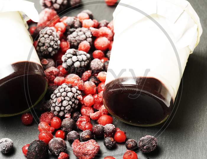 Side View View Of Organic Homemade Yogurts Surrounded By Blackberries And Gorse Fruits On A Black Slate Background. Gastronomy.