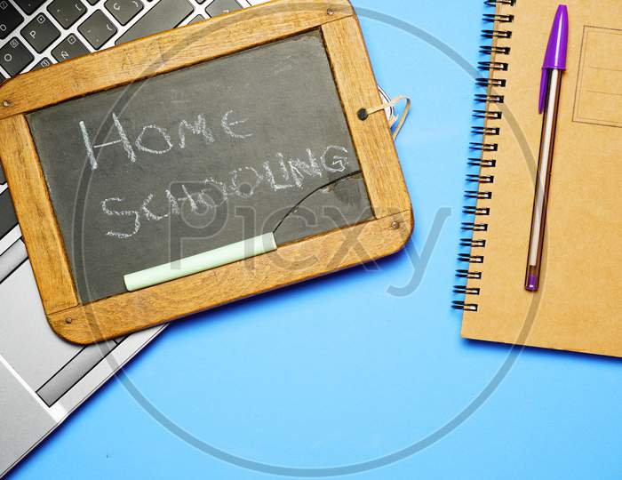 Top View Of Blackboard With Homeschooling Message Next To Notebook Computer And Pen.Covid 19 Home School Concept. Flat Lay