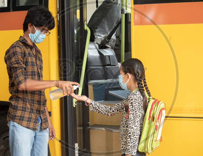 Teacher Providing Hand Sanitizer To Students Before Going Or Getting Inside The School Bus While Maintaining Social Distance As Coronavirus Or Covid-19 Safety Measures.