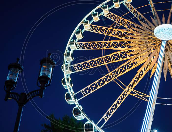 Closeup View Of European Style Street Lamp And Illuminated Ferries Wheel Behind It During Night Time Located In Old Town Over Motlawa River
