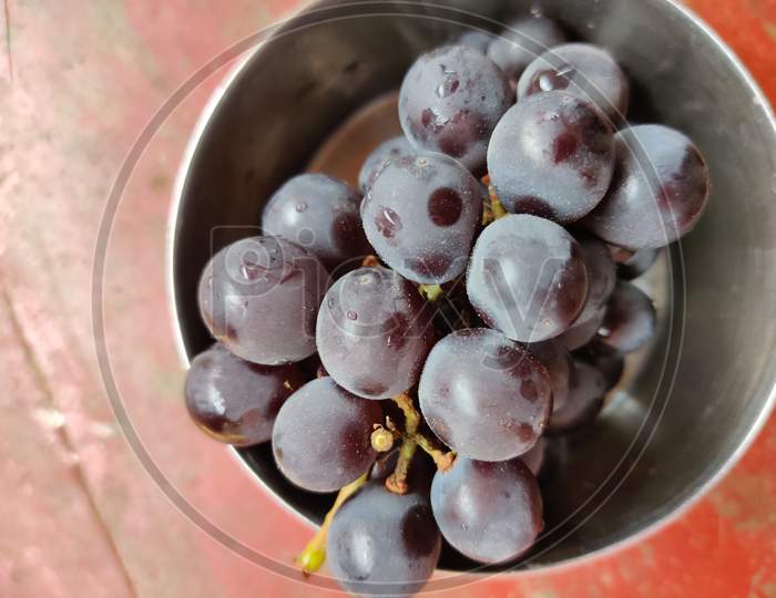 A bunch black Indian grapes kept in steel bowl.