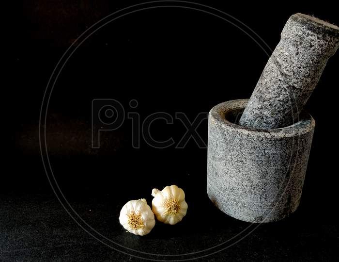 Stone Made Mortar And Pestle With Two Garlics.Isolated On Black Background. Copy Space