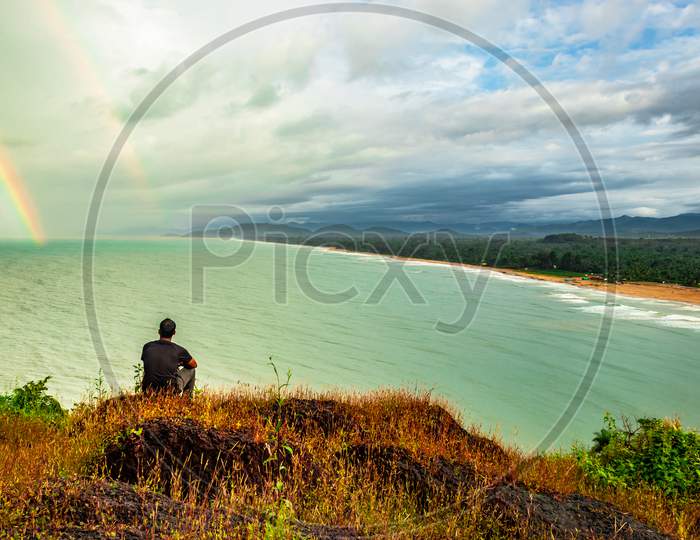 Man Sitting On Hilltop Enjoying Amazing Landscape Of Sea Shore