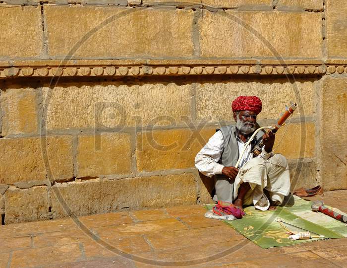 A man wearing turban is siting on ground and playing vilolin at Jaiselmer Rajasthan India