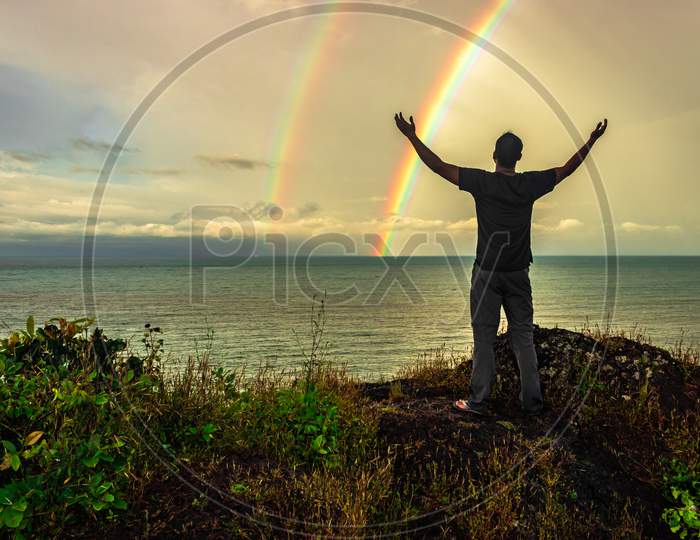 Man At Hilltop Enjoying Amazing Landscape With Rainbow Above Sea Horizon