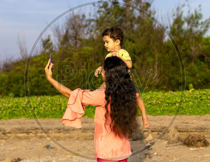 An Asian Mother Seated Her Child On Her Shoulder And Took A Selfie With A Smartphone