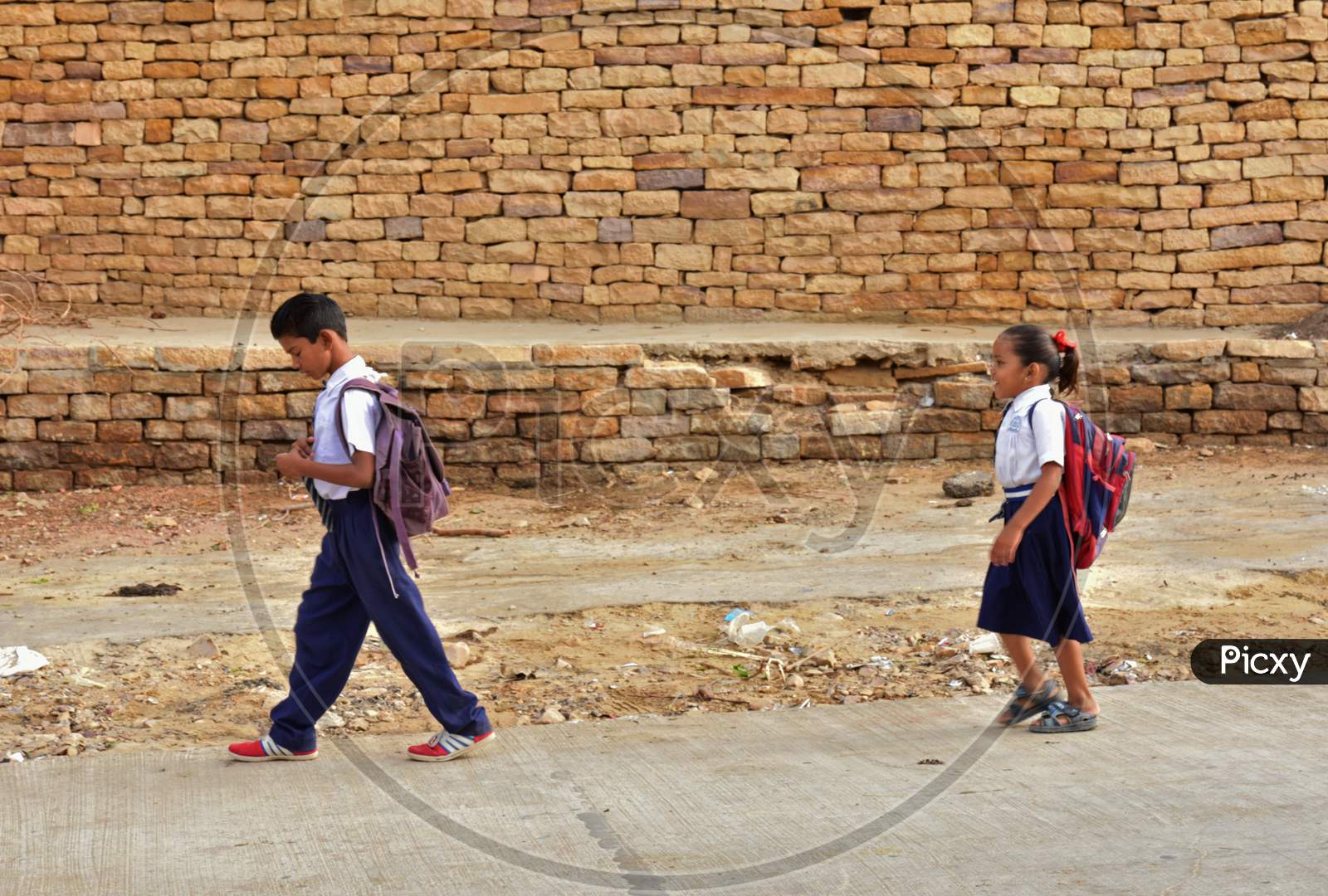 Two Children in their School Dress with school bag on their shoulder heading towards school and the pattern of bricks forming the back ground