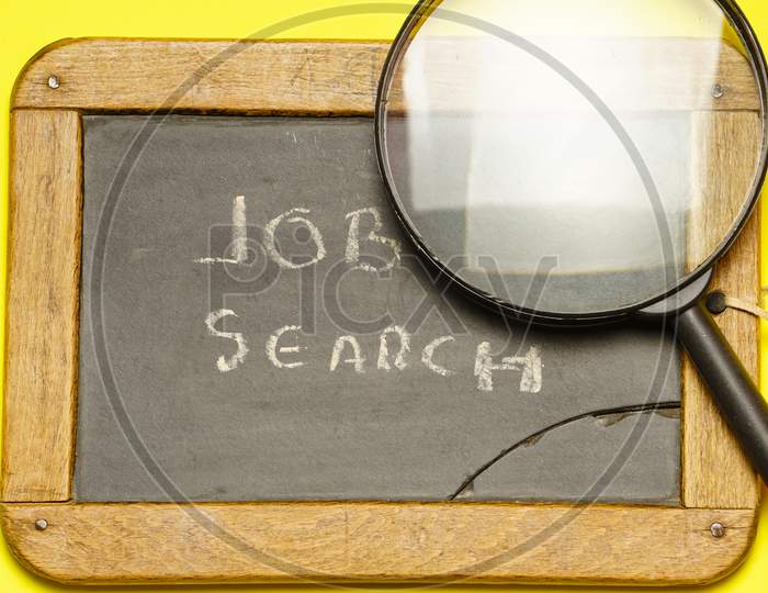 Top View Of Blackboard With Job Search Message With A Magnifying Glass Next To It. Flat Lay