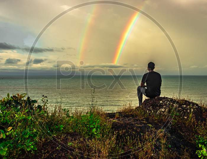Man At Hilltop Enjoying Amazing Landscape With Rainbow Above Sea Horizon