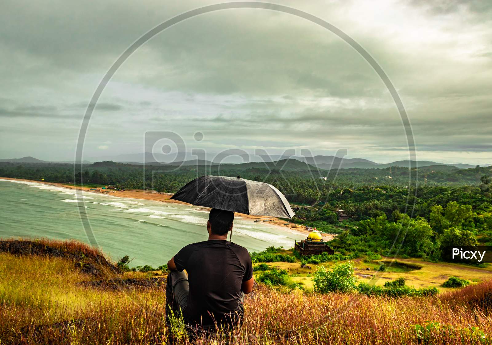 Man Sitting On Hilltop With Umbrella Enjoying Rain With Amazing View