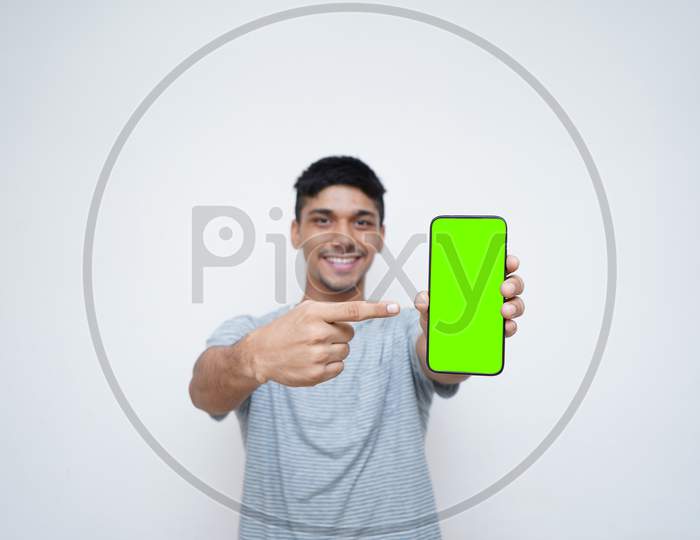 Young Indian Handsome Boy Pointing His Finger Towards His Mobile With Green Screen.Technology And Internet.
