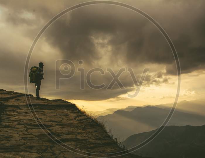 A solo mountain traveller enthralled by the beauty of light coming trough the black cloud