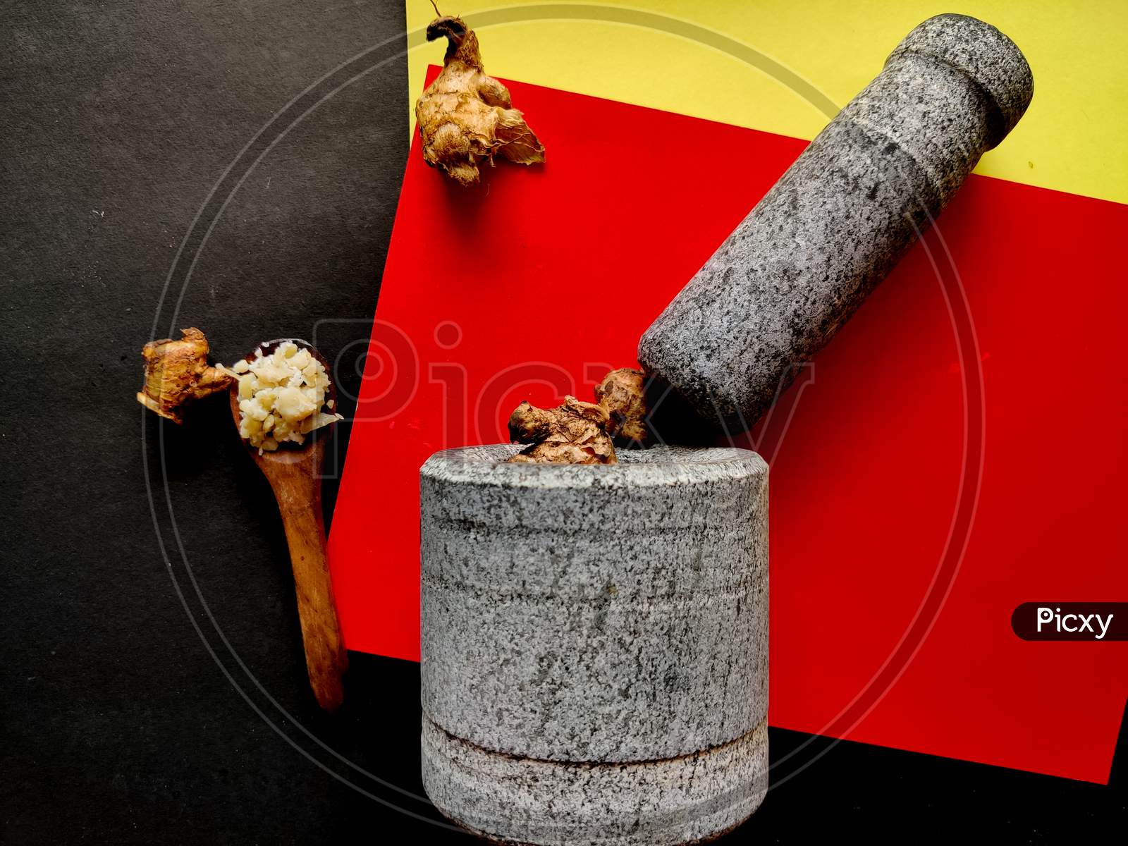 Stone Made Of Mortar And Pestle Is Ready To Crush The Gingers. Isolated On Red, Yellow And Black Background.