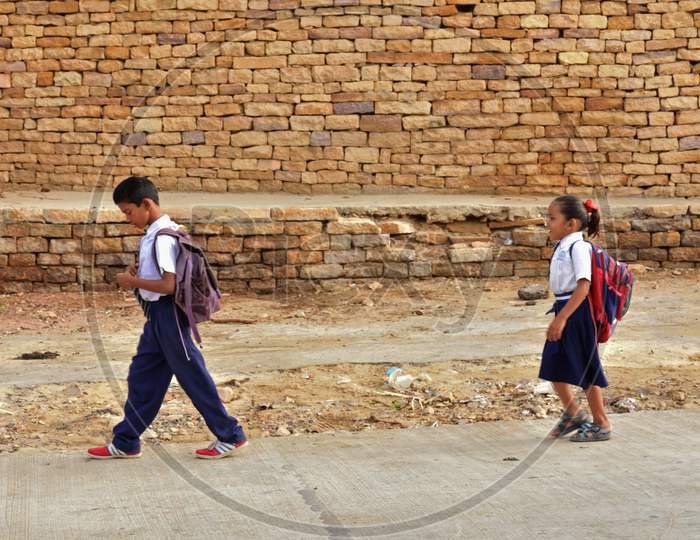 Two Children in their School Dress with school bag on their shoulder heading towards school and the pattern of bricks forming the back ground