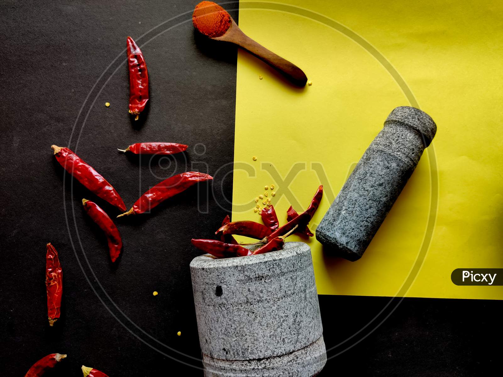Stone Made Of Mortar And Pestle Is Ready To Crush The Red Chillies. Isolated On Yellow And Black Background.