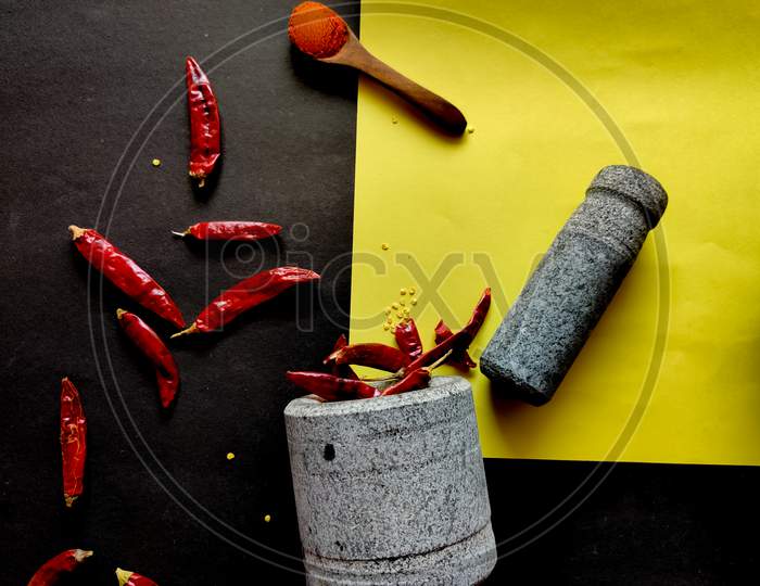 Stone Made Of Mortar And Pestle Is Ready To Crush The Red Chillies. Isolated On Yellow And Black Background.