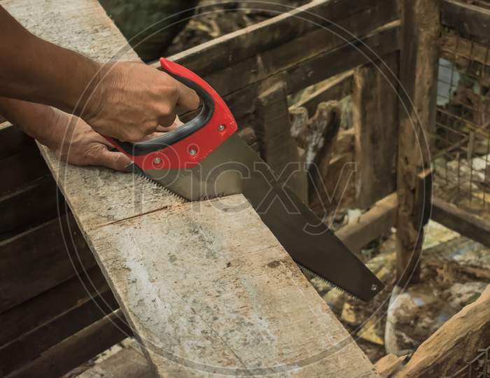 A Man Cutting A Wooden Board With The Help Of A Hand Saw, Carpentry.