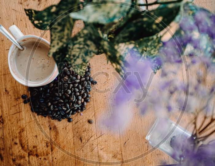 Vintage Flat Lay Of A Cup Of Coffee With Grains Of Coffee Near It And A Plant Decorating Over A Wood Table