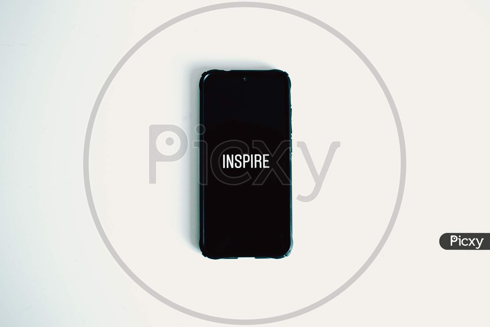 Flat Lay Of A Black Phone Over A White Background With The Word Inspire Written In It