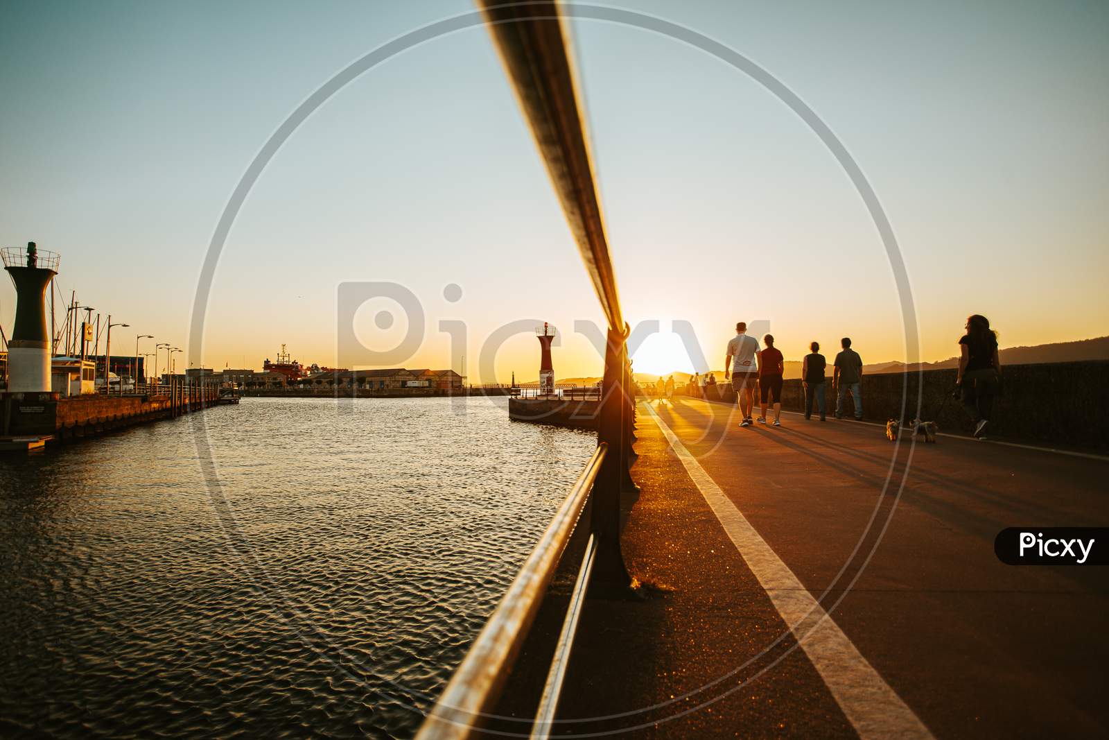 Walk On The Docks To The Lighthouse During A Burning Sunset With People Walking By