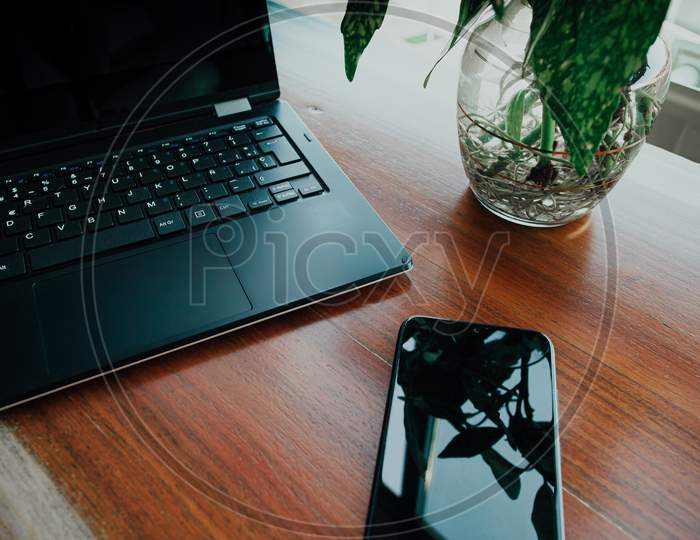 Work Space With A Mobile Phone And A Laptop With A Plant Near Them Over A Wooden Table