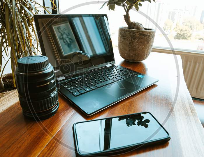 Work Space Composition With A Black Mobile Phone, A Plant, A Photography Lens And A Black Laptop