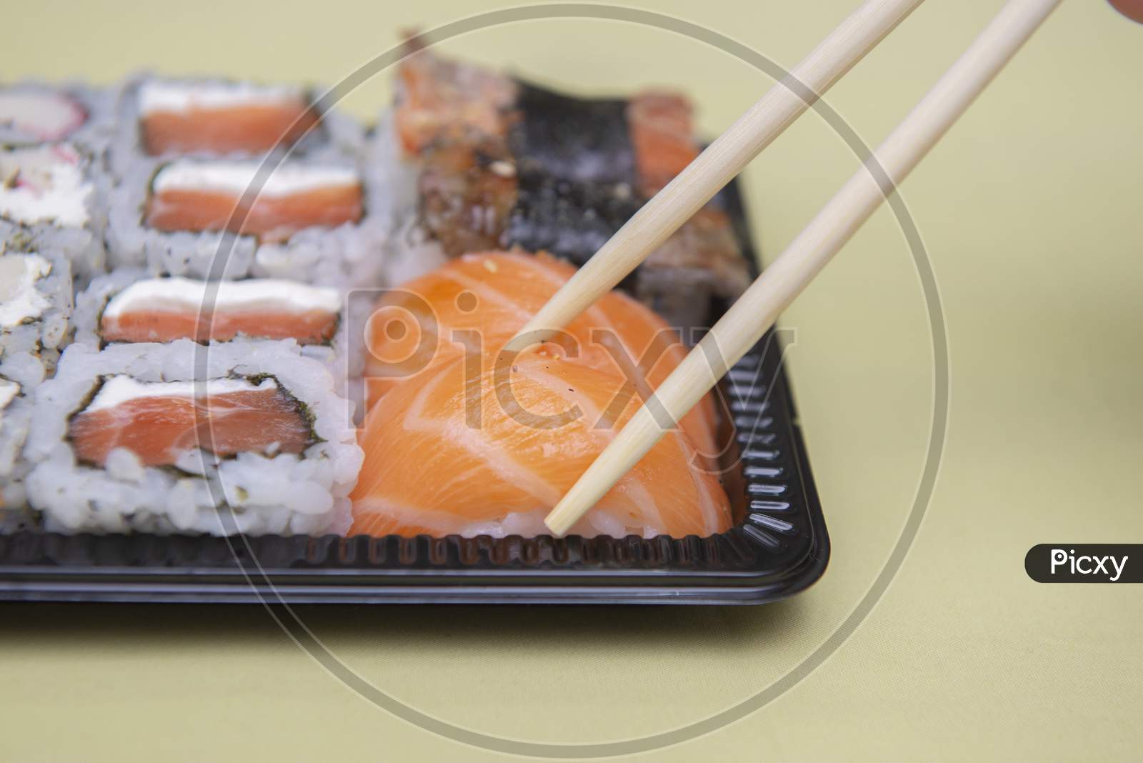 Close Up Of Chopsticks Picking Salmon Niguiri From Black Plastic Tray.