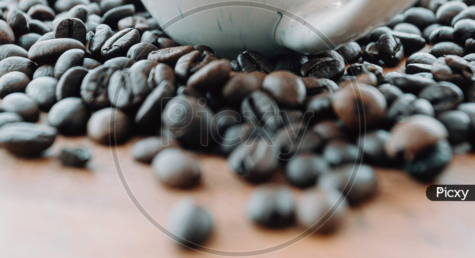Super Close Up Of Some Grains Of Coffee Near A White Cup And Over A Wood Table