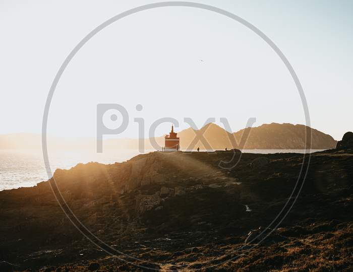 Red Lighthouse In Front Of A Island During A Orange Sunset In The Coast Of Spain During Autumn With Copy Space