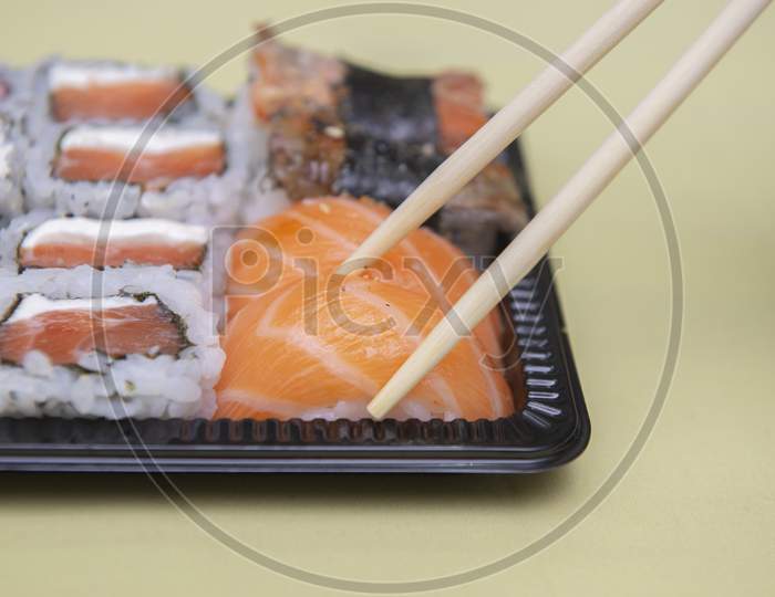 Close Up Of Chopsticks Picking Salmon Niguiri From Black Plastic Tray.