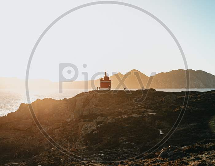 Red Lighthouse In Front Of A Island During A Orange Sunset In The Coast Of Spain During Autumn With Copy Space