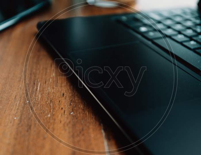 Super Close Up Of The Touch Pad Of The Laptop Over A Wooden Table With A Mobile Phone Near It