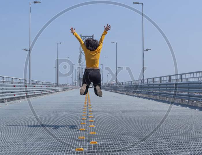 Back View Of Short Haired Woman Jumping, On Steel Bridge Background. Concept Of Happiness And Celebration, Achievement And Freedom.