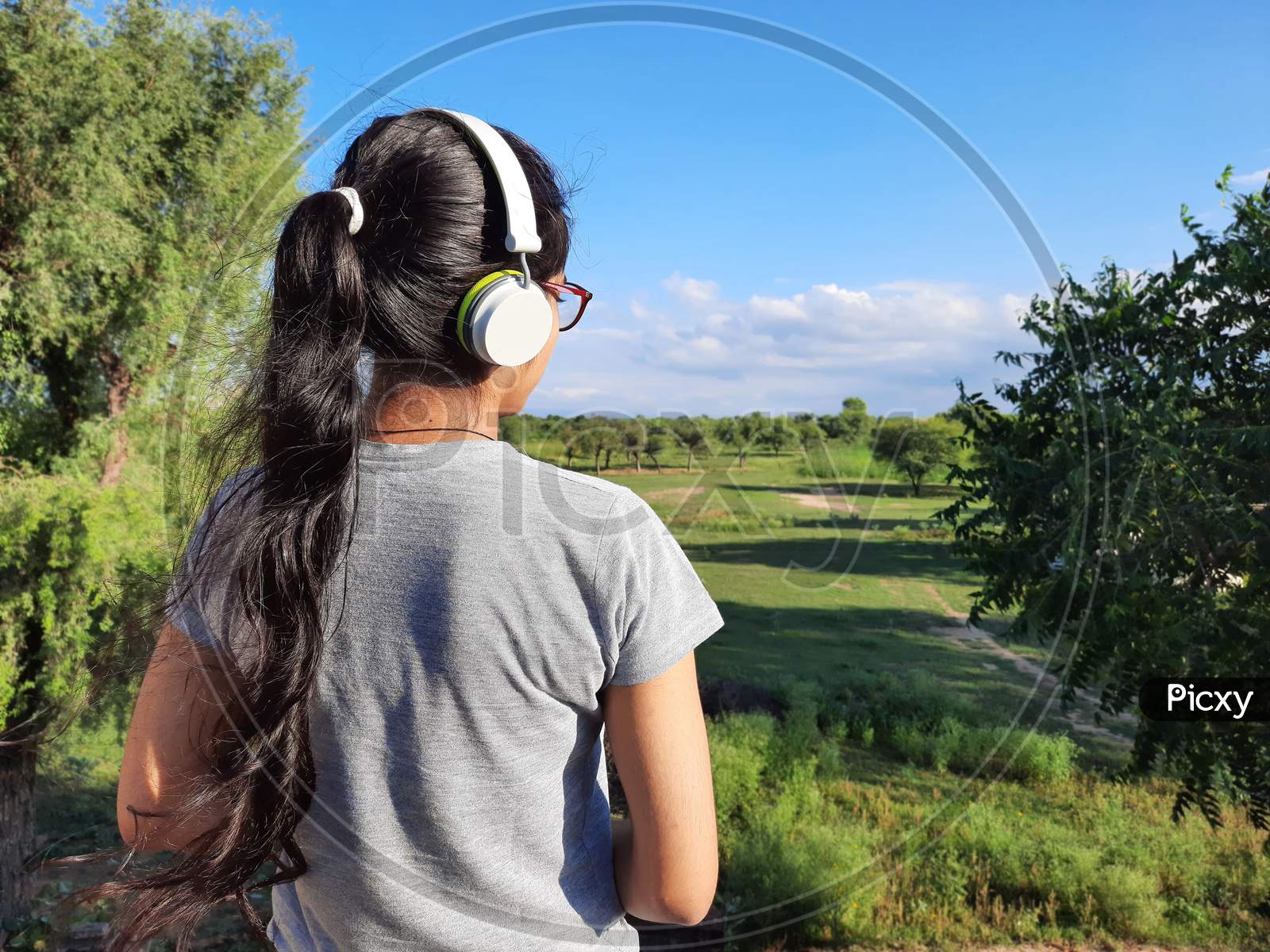 Young Indian Female Listening Music With Headphones Standing In Nature