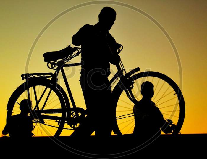 Silhouette of a bicycle and three men on the evening.
