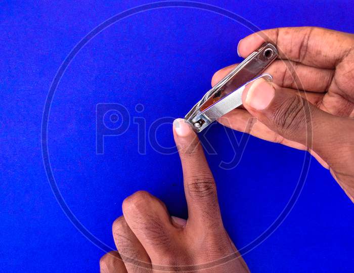 Close Up Of Man Cutting His Fore Finger Nail. Isolated On Blue Background.