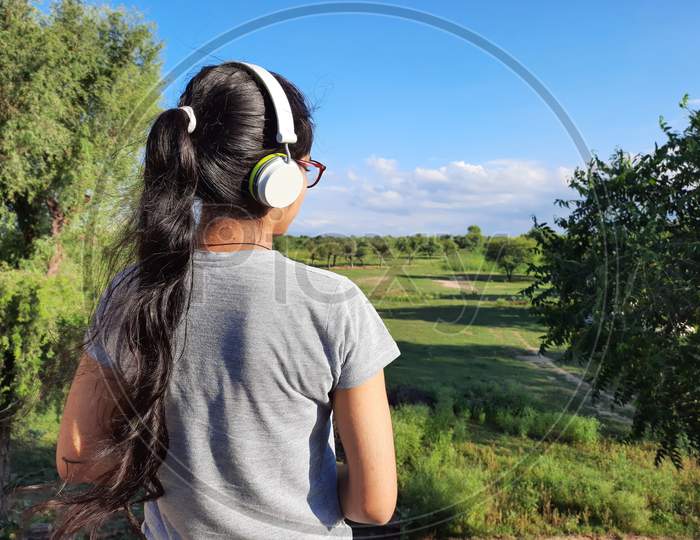 Young Indian Female Listening Music With Headphones Standing In Nature
