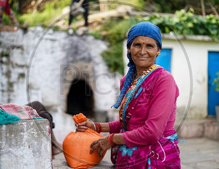 Almora, Uttrakhand / India- June 4 2020 : A Mid Portrait Or An Old Village Woman With Lots Of Wrinkles On Her Face Wearing Pink Blouse With A Sweater, Sitting In A Forest.