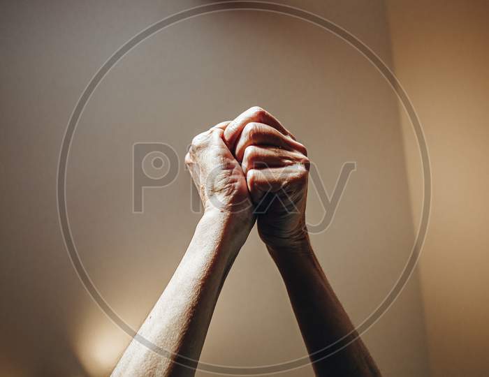 Two Old Woman Hands Rised Grabbing Each Other On Pastel Tones With Lights Surrounding